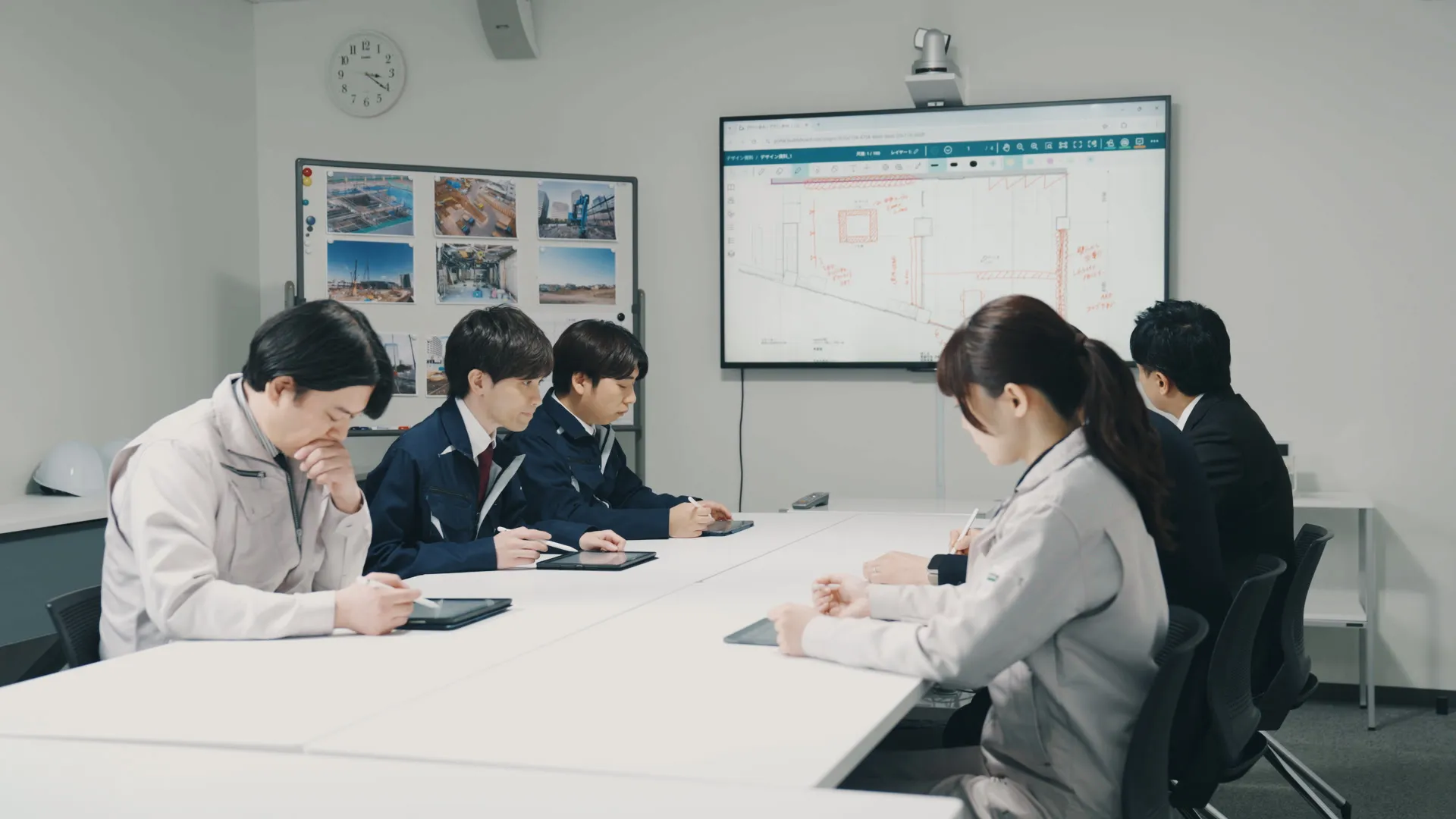 会議室で複数の関係者がタブレットに書き込みながら大型ディスプレイの図面を確認している様子